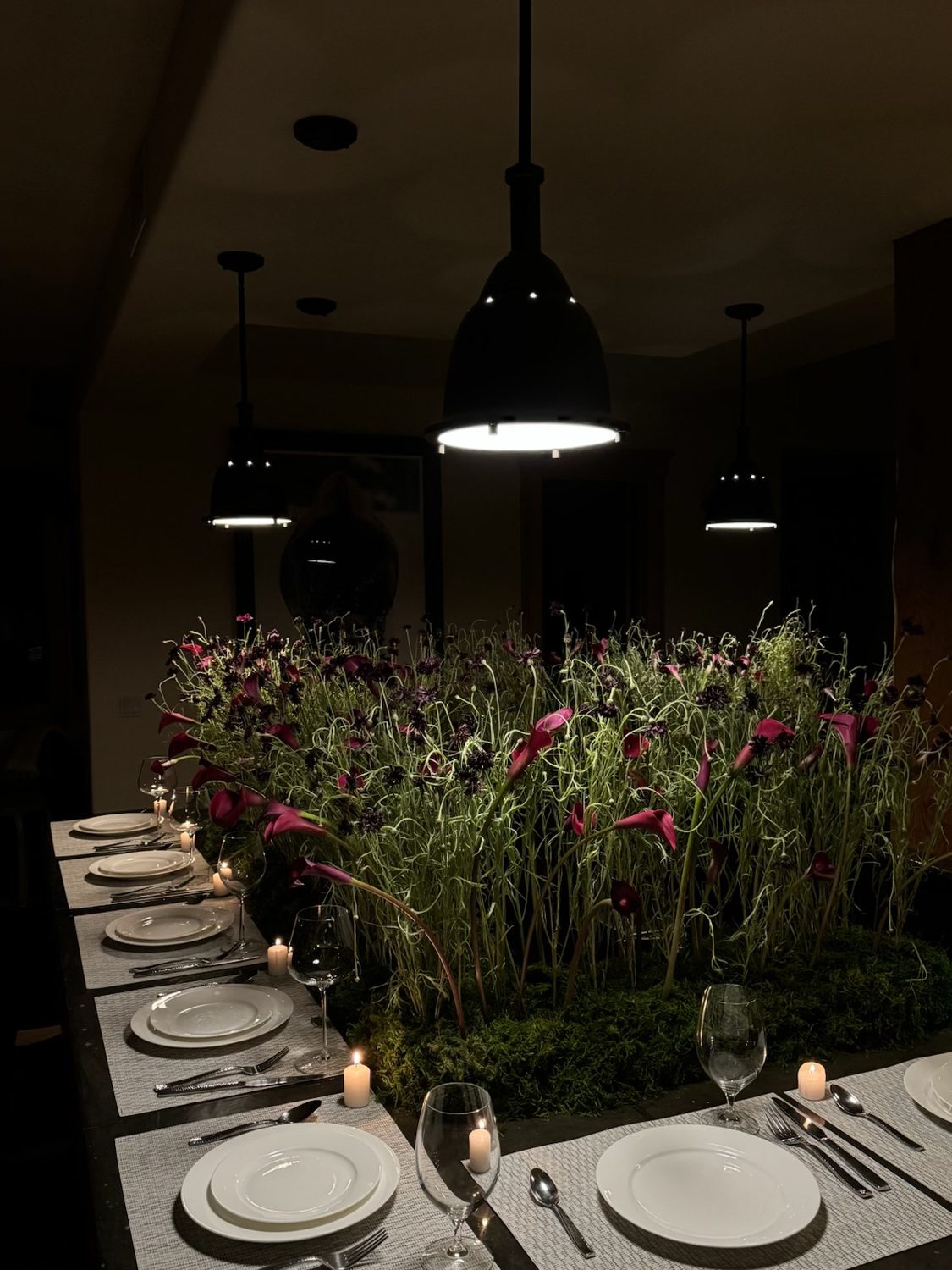 Dramatic dark dinner with a meadow-style centrepiece of calla lilies and cosmos under black pendants, Denver