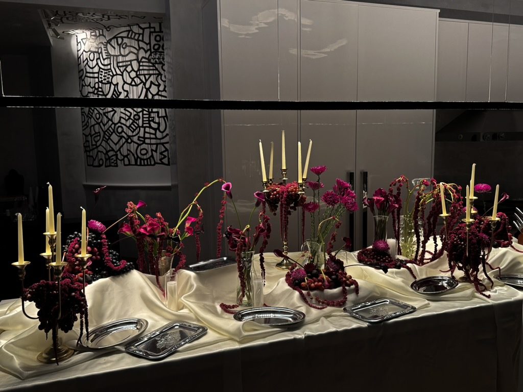 Candlelit table with burgundy amaranth, calla lilies and silver trays against a line-art mural, New York
