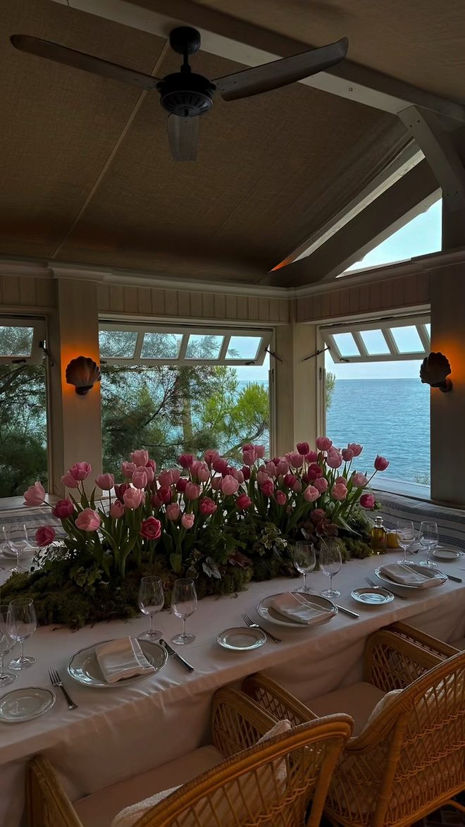 Seaside dining room with pink tulips and a moss runner, open windows to the ocean
