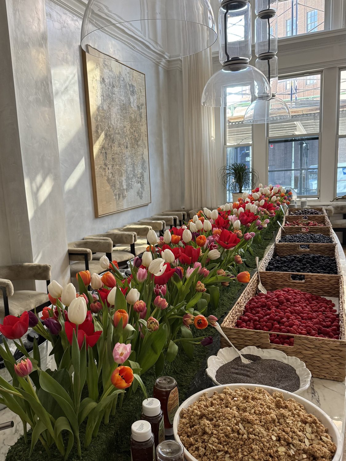 Bright morning table lined with mixed tulips beside baskets of berries and granola, New York, by Kuration Studio
