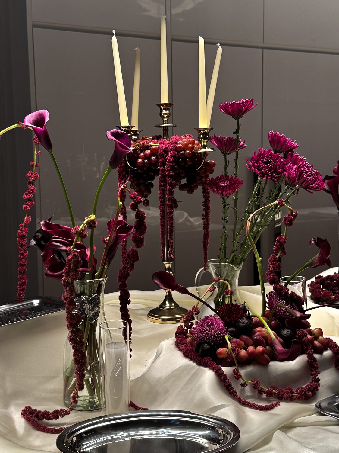 Candlelit table with burgundy amaranth, calla lilies and silver trays against a line-art mural, New York